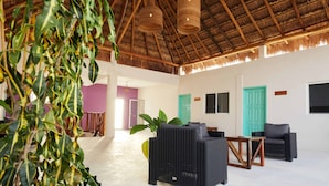 A spacious room with a high thatched ceiling, wicker furniture, and a large plant. - Hotel Pelicano (Chiquilá)