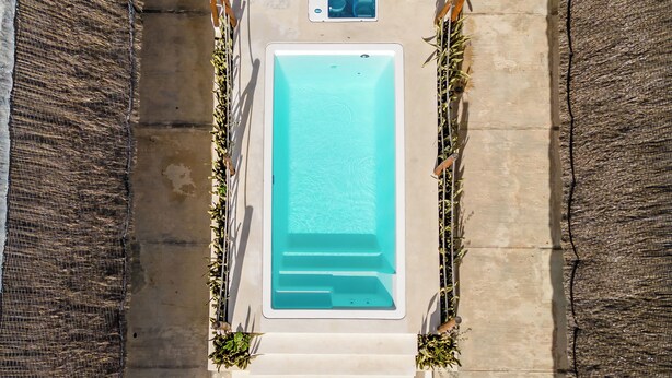 An aerial view of a rectangular swimming pool with two white lounge chairs and a small table on one side. - Hotel Pelicano (Chiquilá)