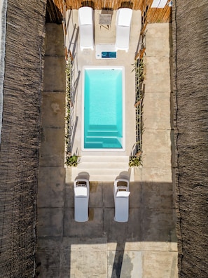 An aerial view of a rectangular swimming pool with two white lounge chairs and a small table on one side.