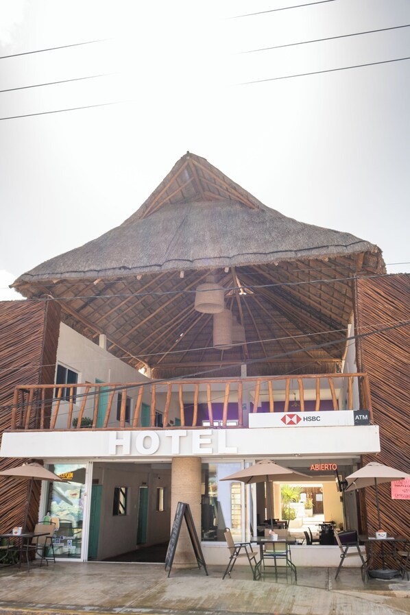 A hotel with a thatched roof, an open terrace with tables and chairs, and a HSBC ATM sign. - Hotel Pelicano (Chiquilá)