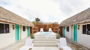 A pool area with lounge chairs and a hot tub, surrounded by thatched-roof buildings with green doors. - Hotel Pelicano (Chiquilá)