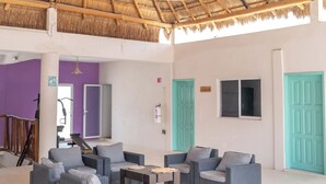A spacious indoor area with a thatched roof, wicker furniture, and a purple wall. - Hotel Pelicano (Chiquilá)