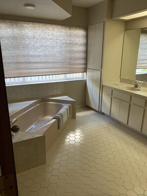 Ein Badezimmer mit einer großen Badewanne, sechseckigen Bodenfliesen und einem Fenster mit Jalousien.