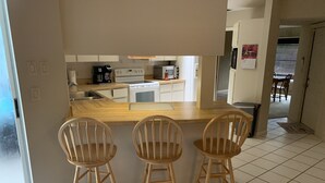 Uma cozinha com bancada de madeira, três banquetas de madeira, fogão, micro-ondas e cafeteira.