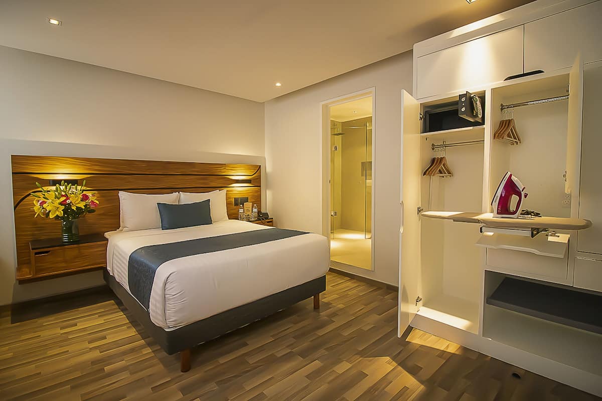 Een moderne hotelkamer met een houten hoofdbord, een groot bed, een nachtkastje, een ingebouwde kledingkast en een inloopkast.