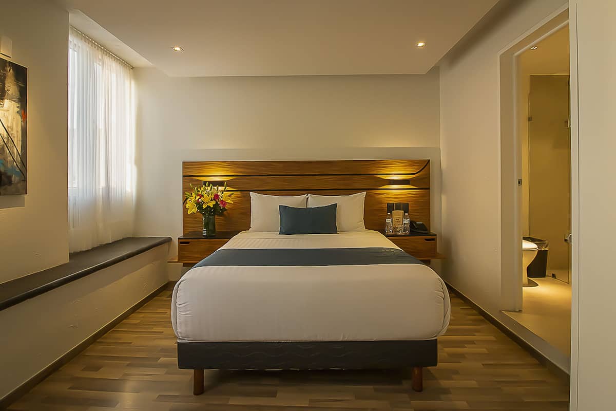 Een moderne hotelkamer met een groot bed, een houten hoofdbord, nachtkastjes, een bloemenvaas en een schilderij aan de muur.