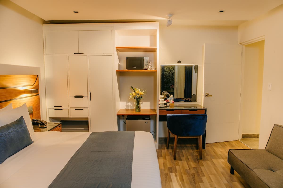 Een hotelkamer met een bed, een bureau, een stoel, een kledingkast en een kleine kitchenette.