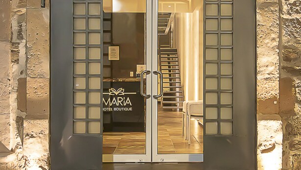 A hotel entrance with a stone facade, a red awning, and a glass door with a sign reading "MARIA HOTEL BOUTIQUE". - Hotel Boutique Maria (Morelia)