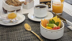 A breakfast setup with a fruit bowl, coffee, and juice on an outdoor table with umbrellas and chairs. - Hotel Boutique Maria (Morelia)
