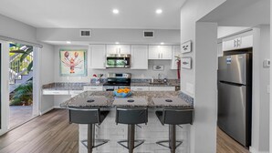 Una cocina moderna con armarios blancos, un refrigerador de acero inoxidable y una encimera de granito.