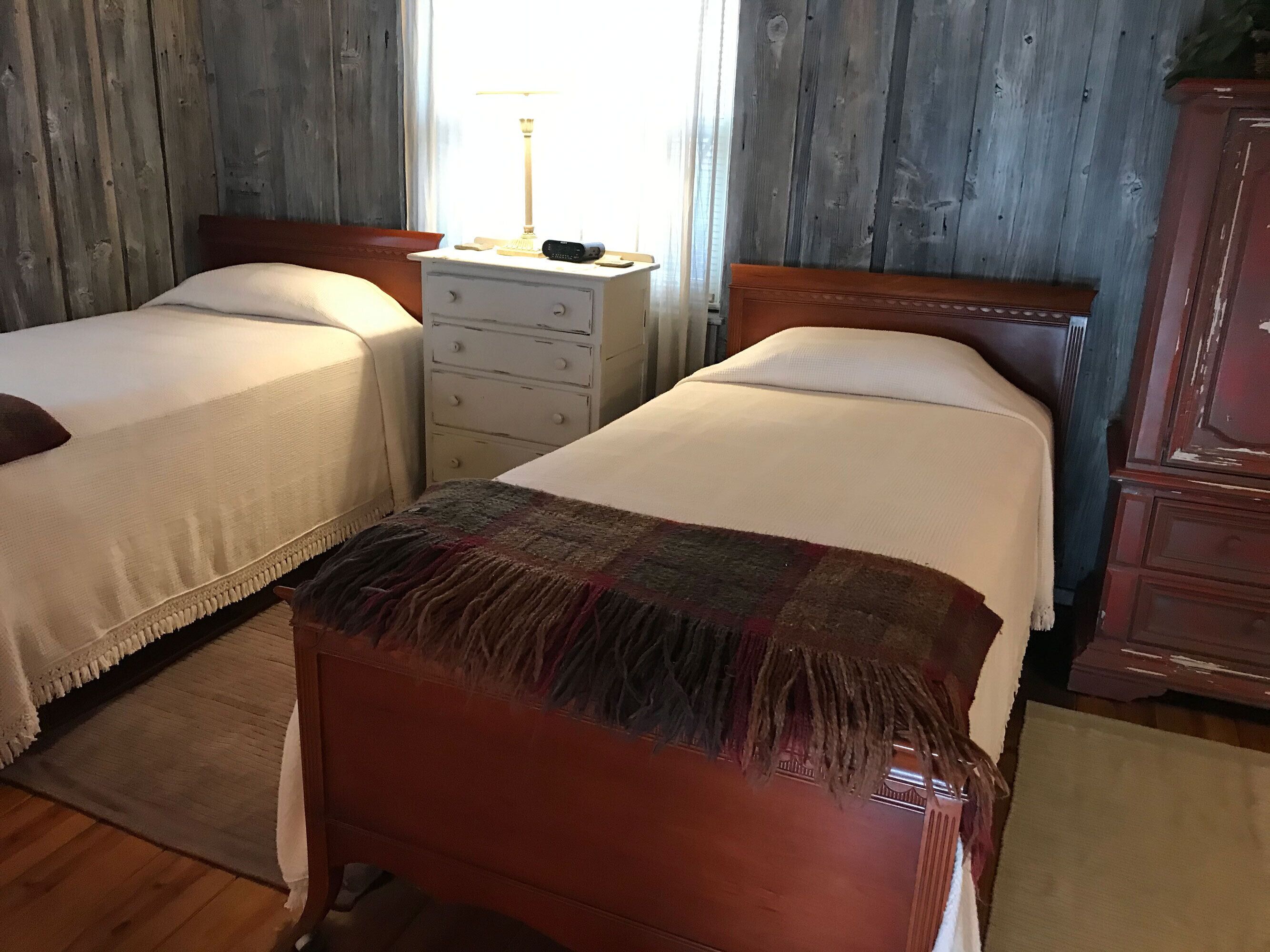 A room with two beds, a wooden dresser, a nightstand, and a lamp.