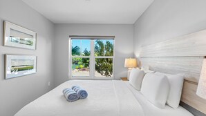 Una camera da letto con una grande finestra, un letto con biancheria da letto bianca e due quadri appesi al muro.