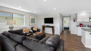 Una sala moderna con un sofá de cuero, una mesa de centro y un televisor. Hay una cocina con armarios blancos y una encimera.