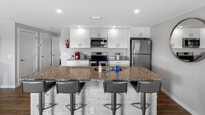 Una cocina moderna con encimeras de granito, electrodomésticos de acero inoxidable y una isla central con taburetes de bar.