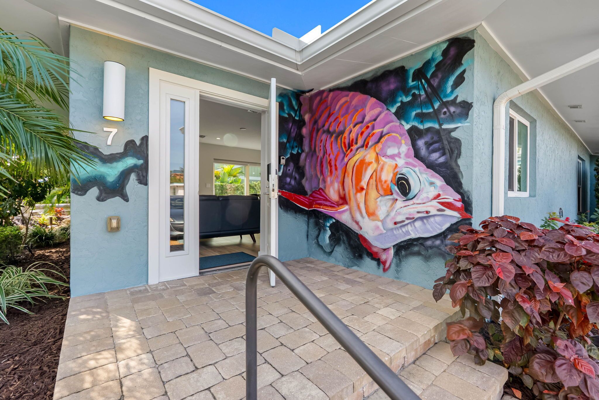 A house with a vibrant fish mural on the exterior wall, a number '7' sign, and a staircase leading to the entrance.