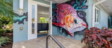 A house with a vibrant fish mural on the exterior wall, a number '7' sign, and a staircase leading to the entrance.
