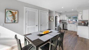 Una cocina moderna con armarios blancos, un refrigerador de acero inoxidable y un comedor con una mesa lista para dos.