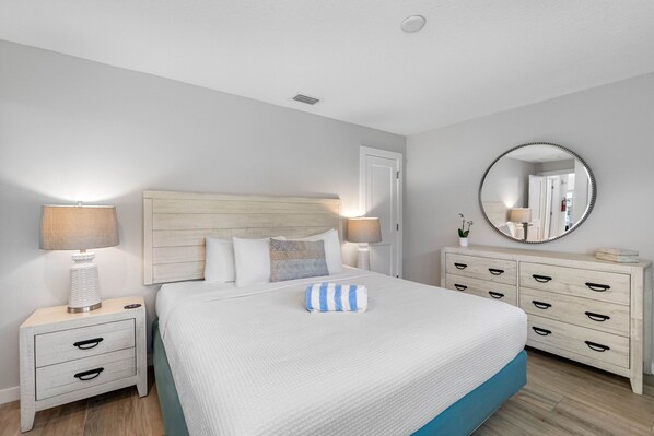 Un dormitorio con cama, mesitas de noche, cómoda, espejo y lámpara.
