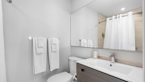 A modern bathroom with a white toilet, a sink with a mirror above it, and a shower curtain. - 3 Bedroom/3 Bath Townhouse - Unit 3 (Nokomis)