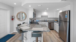 A modern kitchen with white cabinets, a granite countertop, stainless steel appliances, and a round mirror.