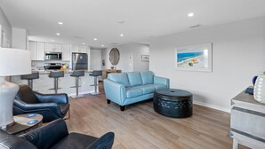 Ein modernes Wohnzimmer mit Sofa, Hocker und Sesseln, ein Küchenbereich mit Geräten sowie eine Essecke.
