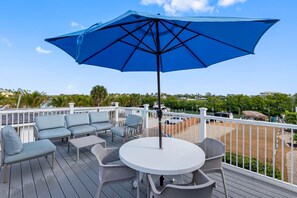 Una terraza con mobiliario exterior, incluyendo una mesa redonda y sillas, y un gran paraguas azul.