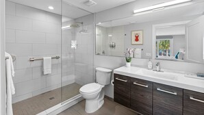 Ein modernes Badezimmer mit einer Duschkabine aus Glas, einer weißen Toilette und einem Waschtisch mit dunklen Holzschränken.