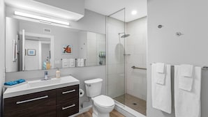 Een moderne badkamer met een douchecabine van glas, een wit toilet, een donker houten wastafelmeubel en een grote spiegel.