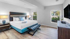 A modern bedroom with a large bed, a bench, a desk, and a TV.