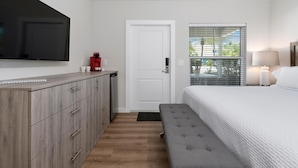 Une chambre à coucher comprenant un lit, un téléviseur fixé au mur, une armoire, une porte et une fenêtre avec des stores.