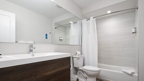 A modern bathroom with a wooden vanity, a toilet, a bathtub, and a shower curtain. - Hotel Studio (Ground Level) - Unit C (Nokomis)