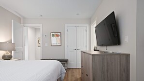 A bedroom with a bed, a dresser, a television, and a door. - Hotel Studio (Ground Level) - Unit C (Nokomis)