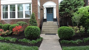 A two-story brick house with a blue front door, a small front yard with shrubs and a tree, and a mailbox at the entrance. - Bright, Parkside condo with pool (Louisville)