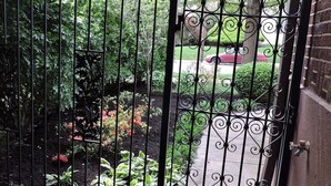 A gated entrance with a metal gate, a brick wall, and a garden with various plants and flowers. - Bright, Parkside condo with pool (Louisville)