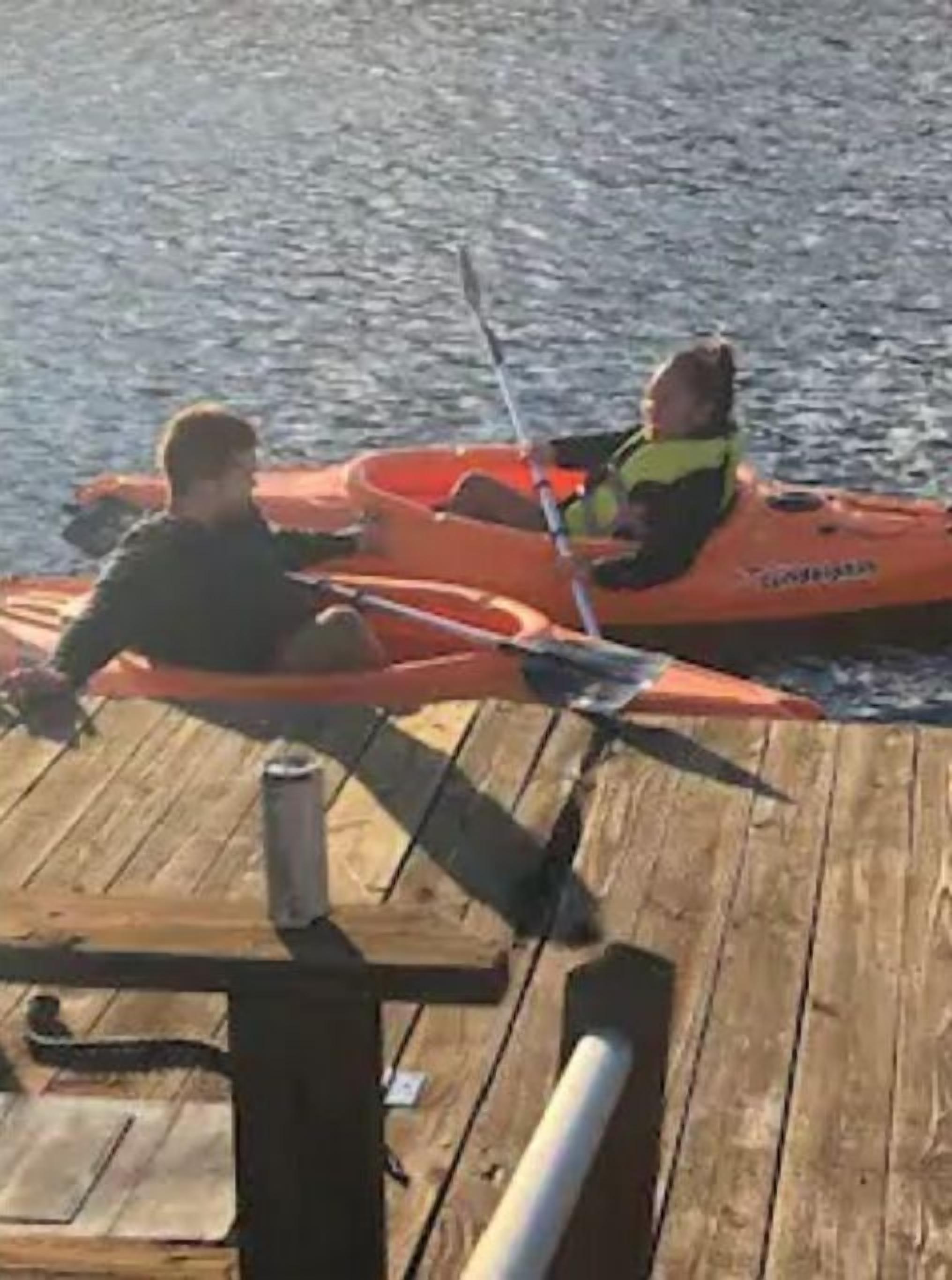 A wooden dock with two kayaks and a person fishing.