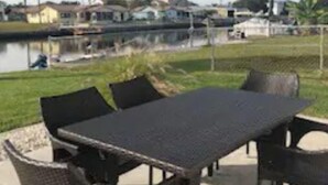 An outdoor patio with a table and chairs, a view of a body of water, and houses in the background. - The Mermaid Beach House 2 (Hernando Beach)