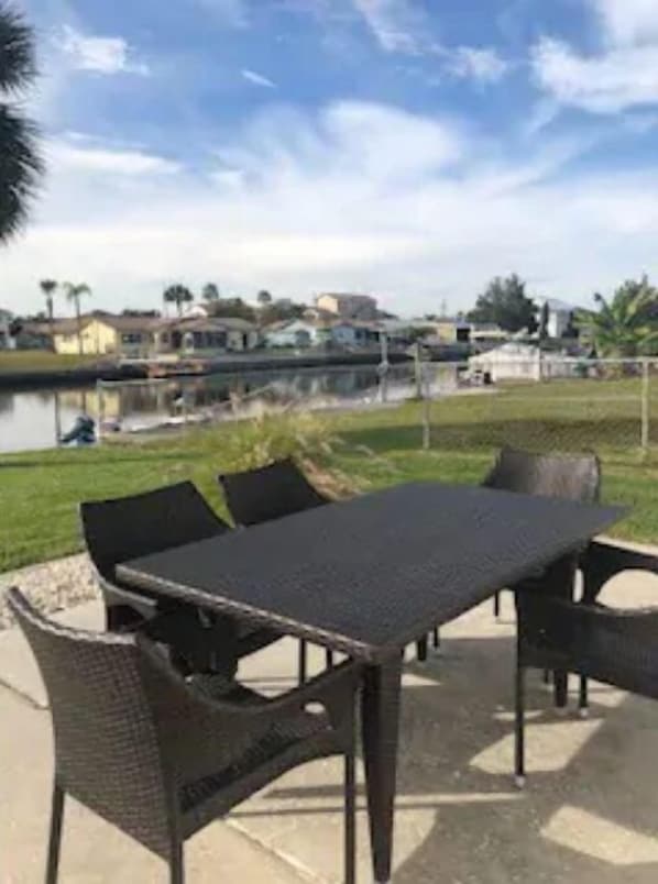 An outdoor patio with a table and chairs, a view of a body of water, and houses in the background. - The Mermaid Beach House 2 (Hernando Beach)