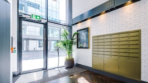 A modern lobby with a large potted plant, a glass door entrance, and a wall-mounted mailbox. - Hilltop Serviced Apartments - Piccadilly (Manchester)