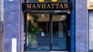 The exterior of a building with a black entrance and the name "MANHATTAN" in gold letters above the doors. - Hilltop Serviced Apartments - Piccadilly (Manchester)