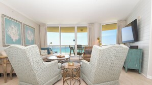 Un salon avec des fauteuils à motifs, une table basse ronde et un téléviseur fixé au mur.