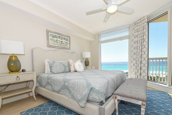 A bedroom with a bed, bedside tables, a bench, a ceiling fan, and a view of the ocean. - Beachfront chic condo w/ beach service in the heart of Destin! 🌊🌅🐚 (Destin)