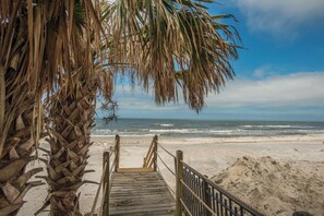 A wooden boardwalk leading to a sandy beach with ocean waves in the background.
