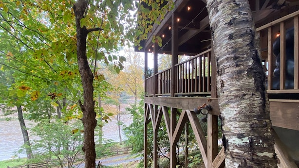 A wooden deck with a railing overlooking a rocky stream and a forested area. - 10 Star River Front Retreat - Water Sports, Hiking, Campfires by the River (Sparta)
