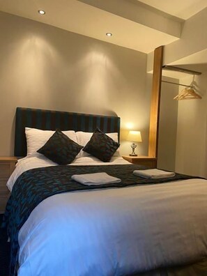 A hotel room with a bed, a bedside table with a lamp, and a mirror on the wall. - The Silk House (Leek)