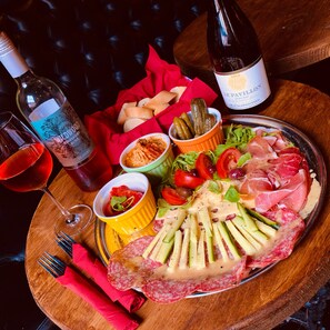 A charcuterie board with various meats, cheeses, and vegetables, accompanied by wine bottles and glasses. - The Silk House (Leek)