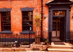 A red brick building with a black metal fence, a door, and windows. - The Silk House (Leek)