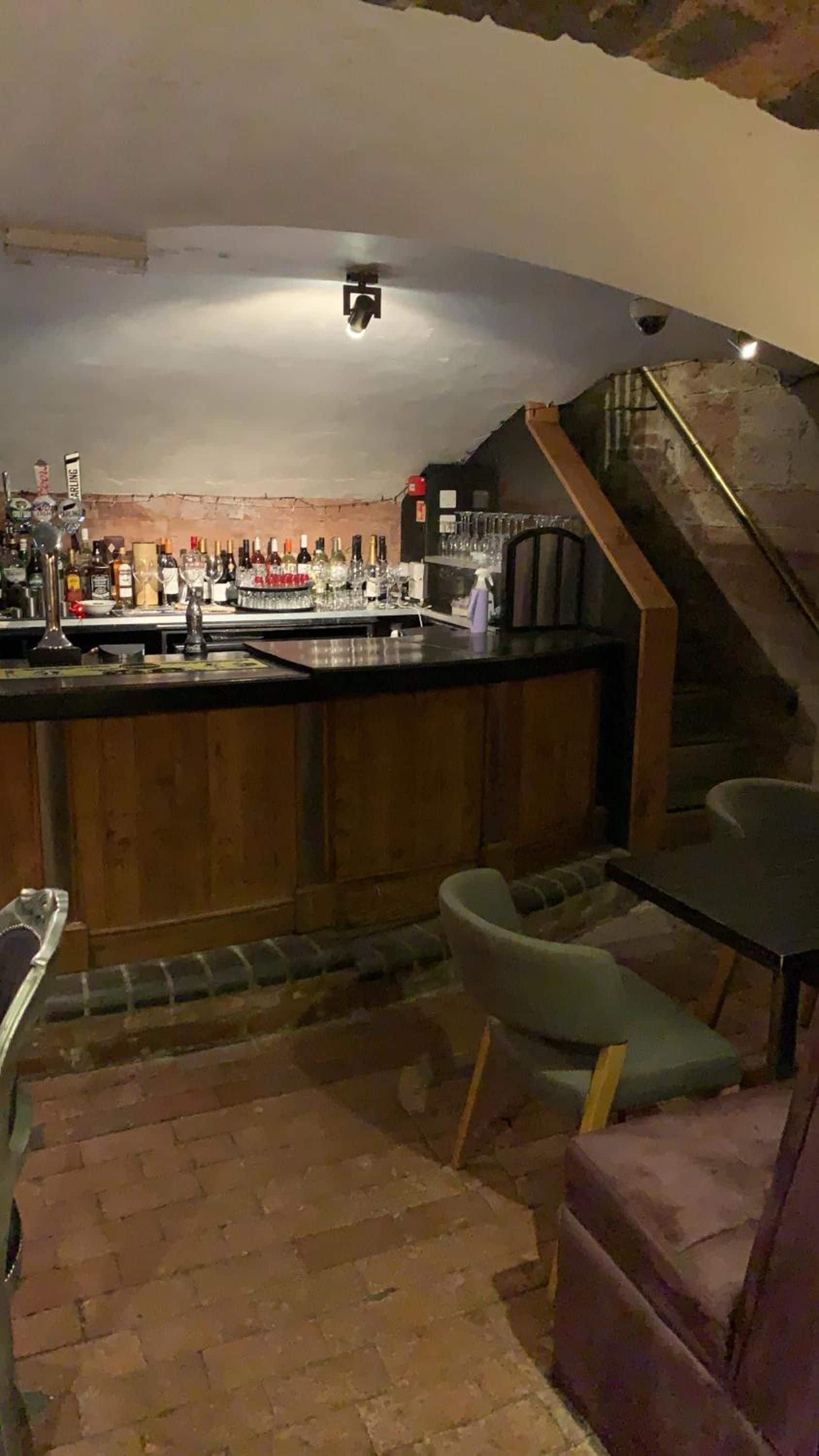 Zona de bar con mostrador, taburetes y una escalera que sube a un nivel superior.