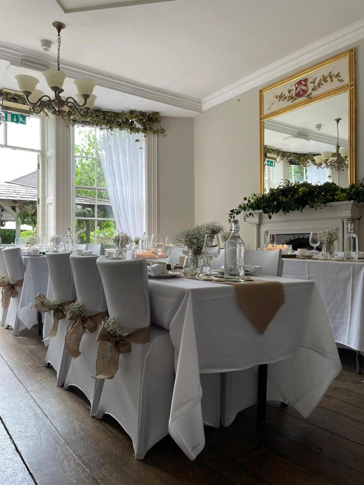 A formal dining room with round tables, white tablecloths, and chairs with bows.