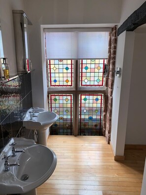 A narrow bathroom with two sinks, a mirror, and a stained glass window. - The Silk House (Leek)