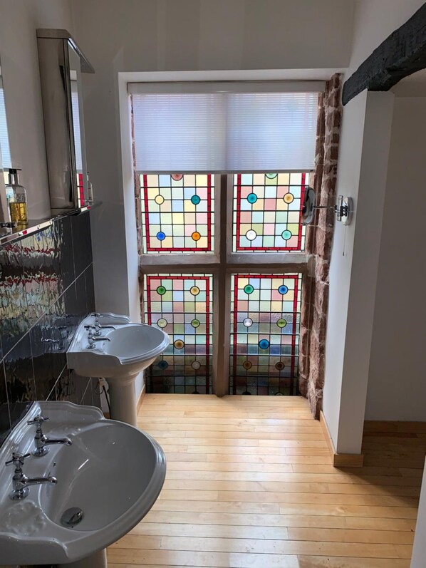 A narrow bathroom with two sinks, a mirror, and a stained glass window.